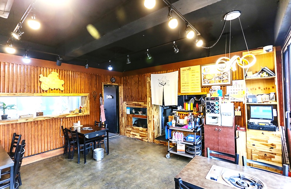 테이블이 넓게 배치되어 있고, 검은색 천장에 조명이 달려있고, 우드 벽면으로 차분함을 주는 문어물갈비 대구본점 실내 인테리어