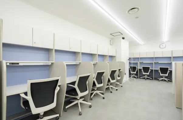 재수학원- 흰색공간 벽쪽 파란색 벽면의 책상에 흰색 바퀴의자가 꽂아져 있는 독서실