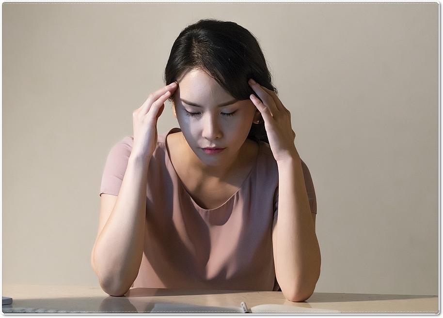 관자놀이 부근에 두 손을 가져다 댄 채 두 눈을 감고 다소 피곤한 표정을 짓고 있는 여성의 모습