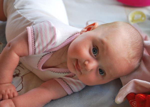 볼과 팔에 붉은기가 올라온 아기가 바닥에 엎드려 누운 채 정면을 바라보는 모습, 태열이 의심되는 여름철 피부 상태