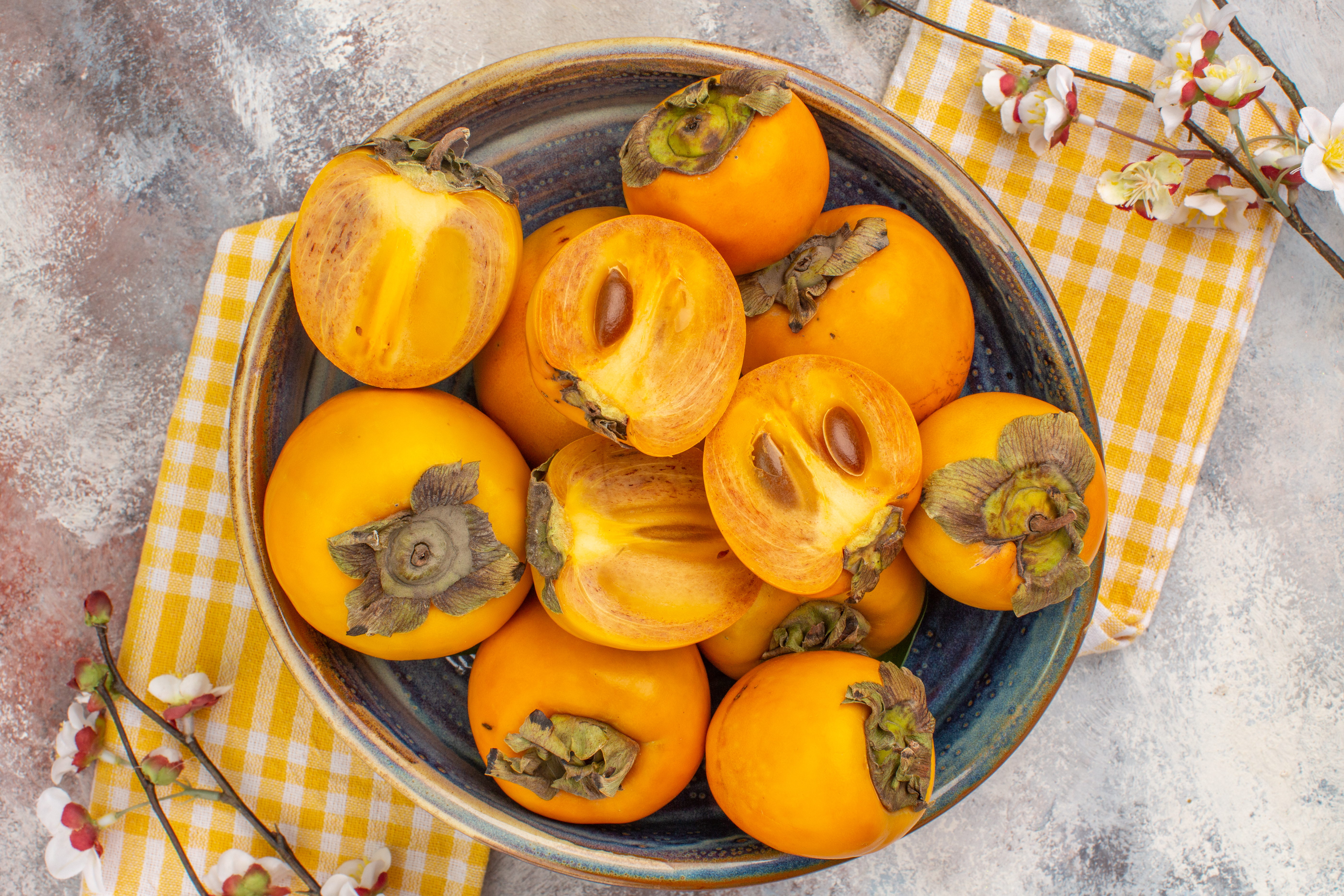 top-view-delicious-persimmons-bowl-yellow-kitchen-towel-apricot-blossom-branch-nude-background1