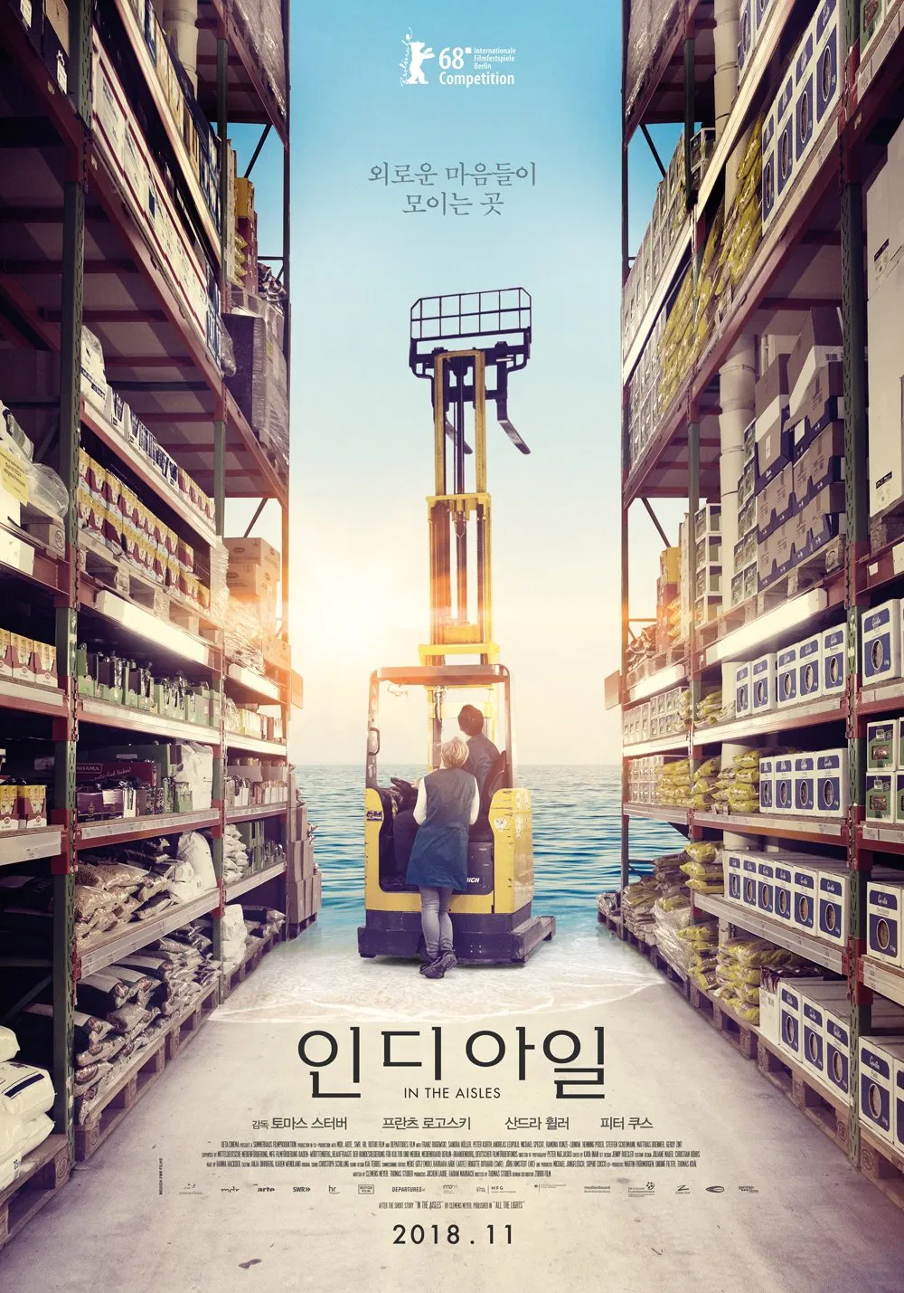 영화 <인 디 아일> 포스터. 대형 창고형 마트의 진열대 사이, 포크리프트 위에 두 남녀가 서 있고, 배경은 푸른 바다와 노을이 어우러진 초현실적 풍경이다.