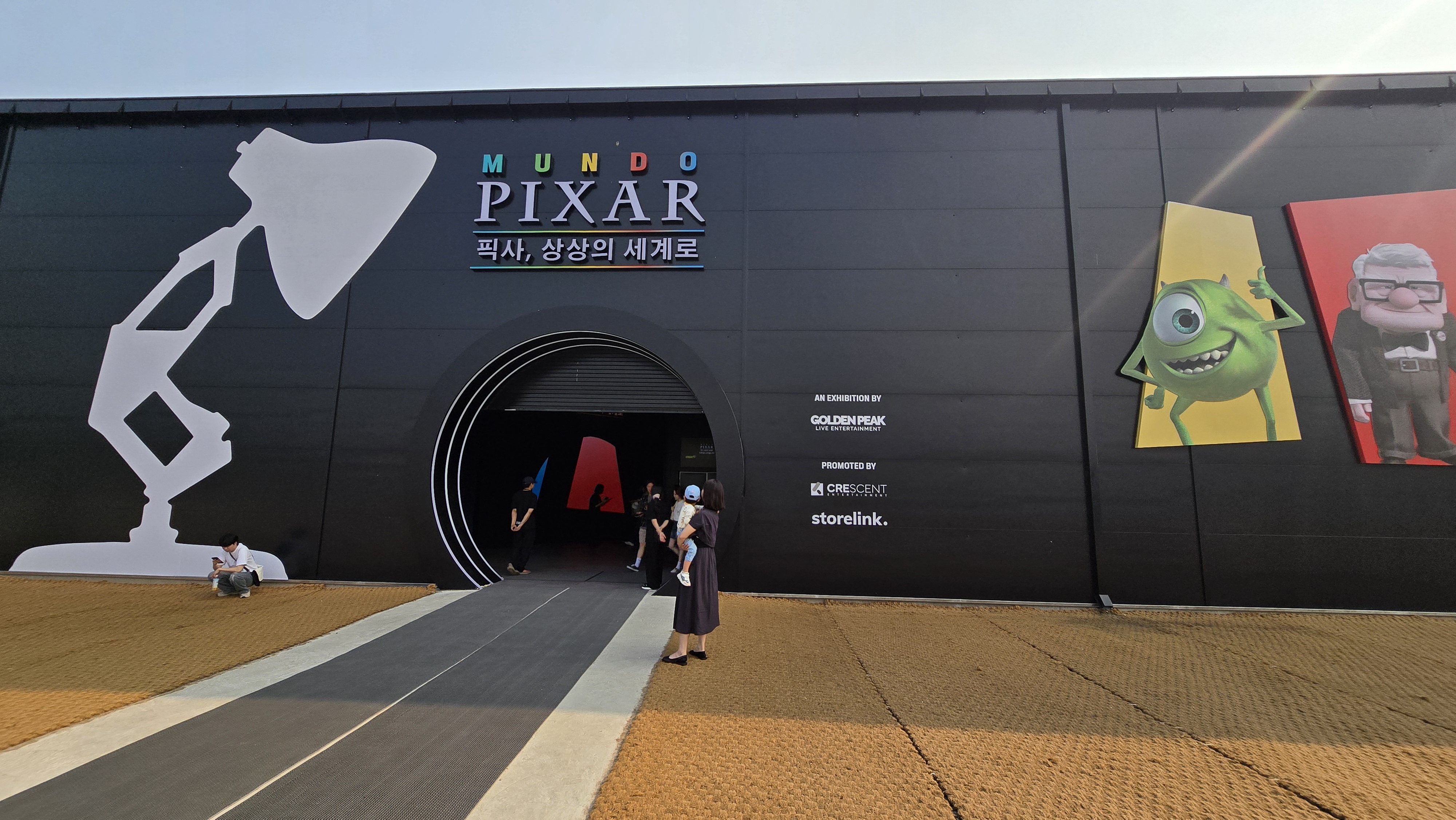 문도 픽사 서울 전시회 입구 전경. 픽사 램프, 몬스터 주식회사 마이크, 업의 칼 할아버지 캐릭터가 외벽에 장식되어 있다.