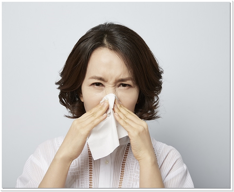 휴지로 코를 막고 찡그린 표정을 짓고 있는 여성의 모습
