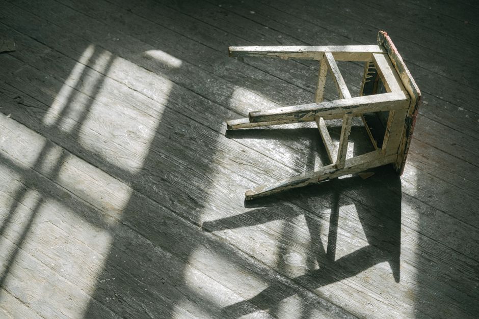 A worn wooden stool casting shadows on a sunlit wooden floor, creating a rustic and moody ambiance.