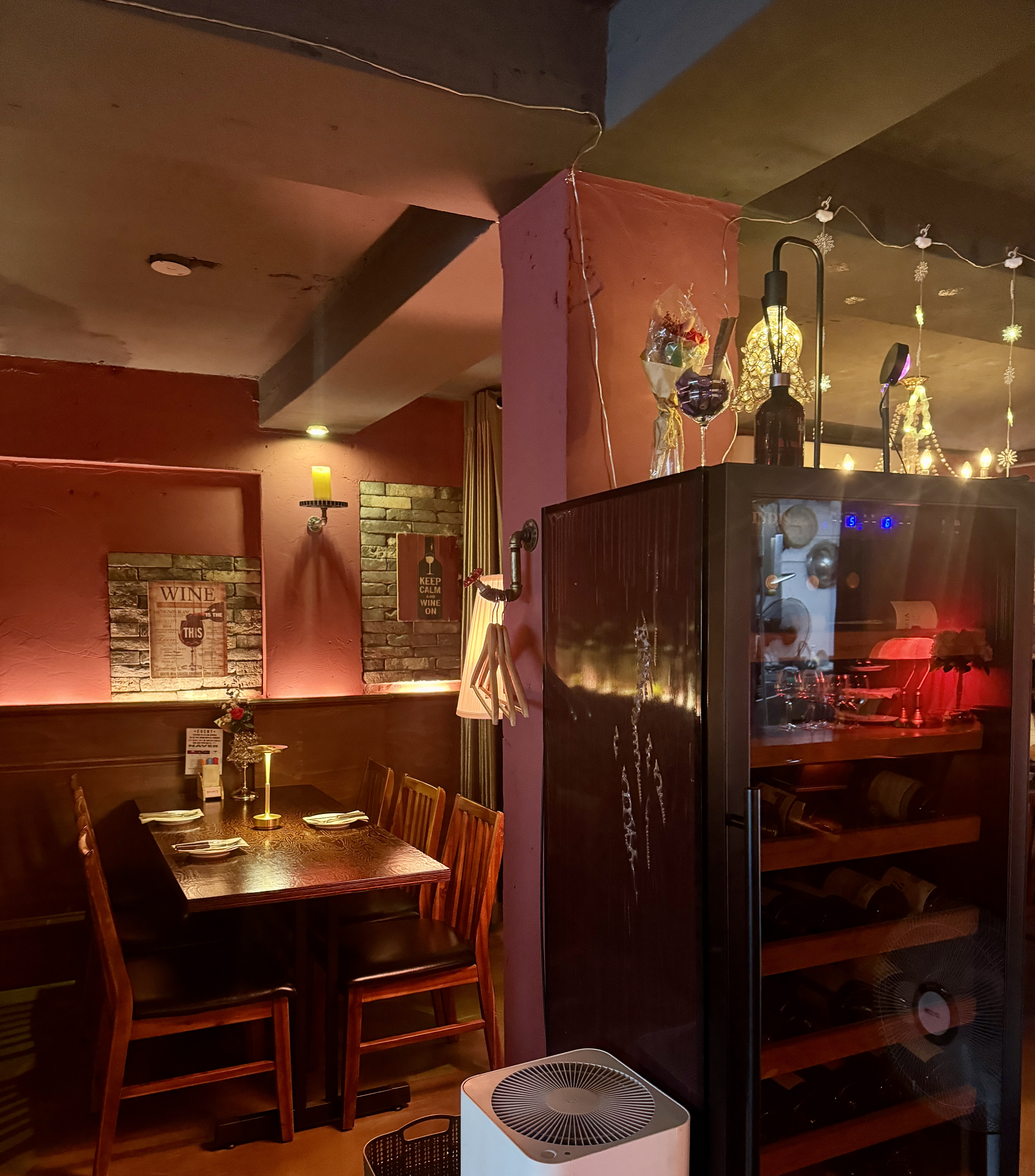 논현 와인바의 테이블 좌석과 와인셀러. 따뜻한 간접조명과 소박한 인테리어가 아늑한 분위기를 더해준다.