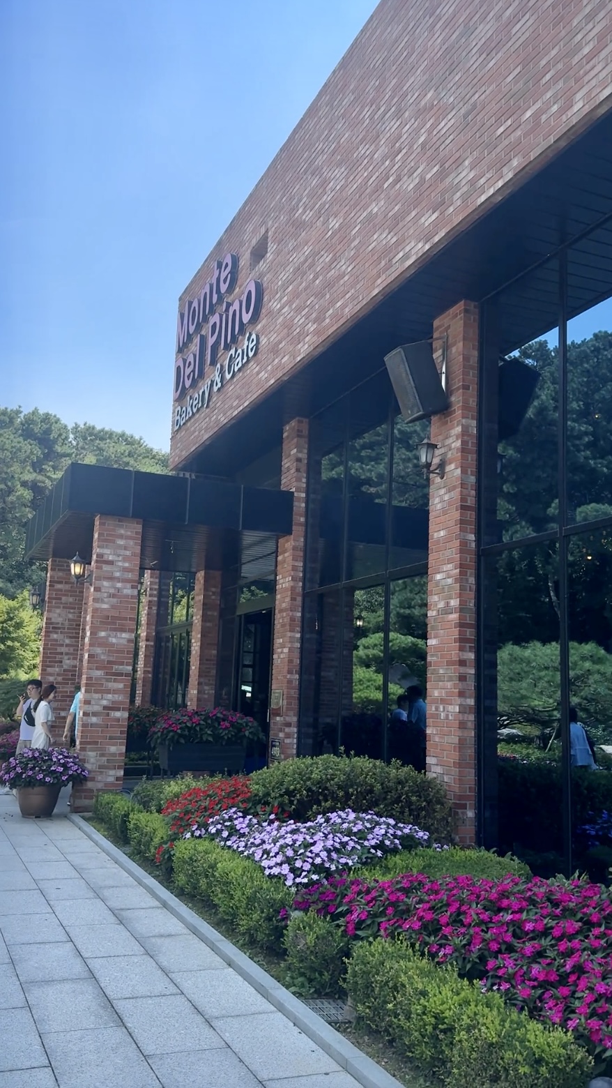 포 카페 Monte Del Pino의 벽돌 외관과 유리창, 입구 주변을 가득 채운 화사한 꽃들