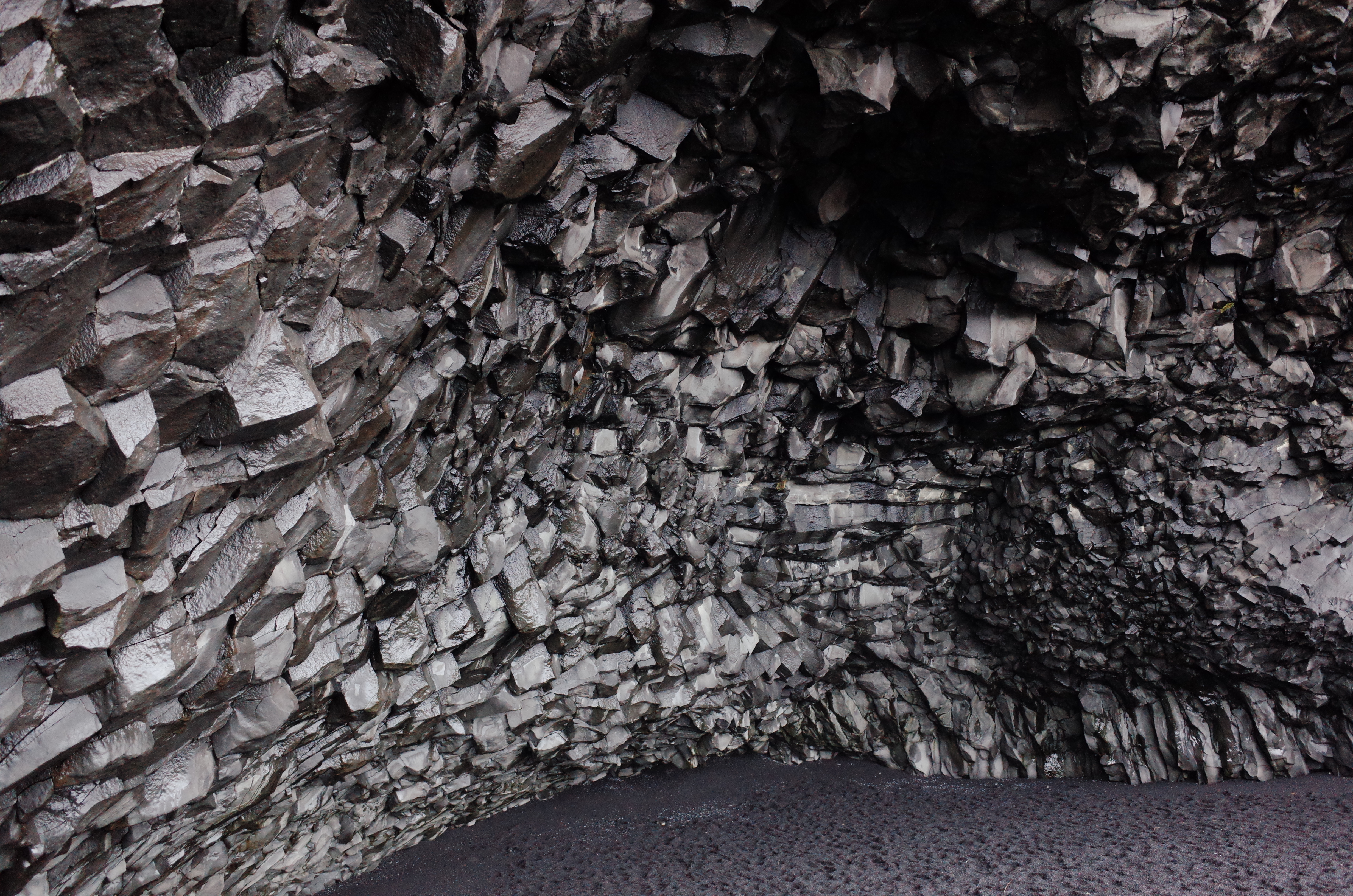 거칠고 어두운 질감의 현무암 기둥들이 동굴 천장을 이루고 있는 아이슬란드 레이니스피아라 해변의 독특한 절벽 구조