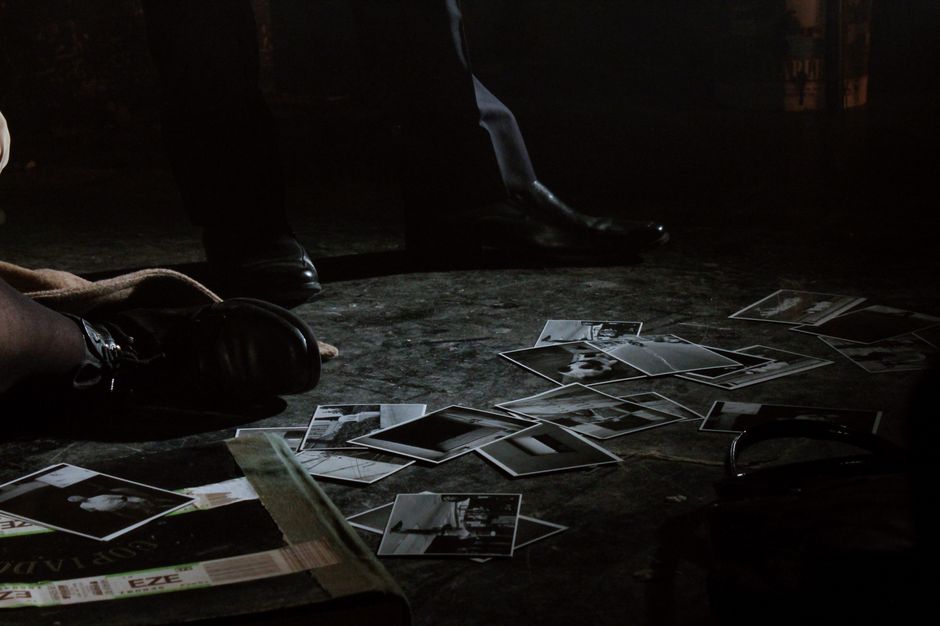 Moody scene featuring scattered black and white photographs and feet on a dimly lit floor.