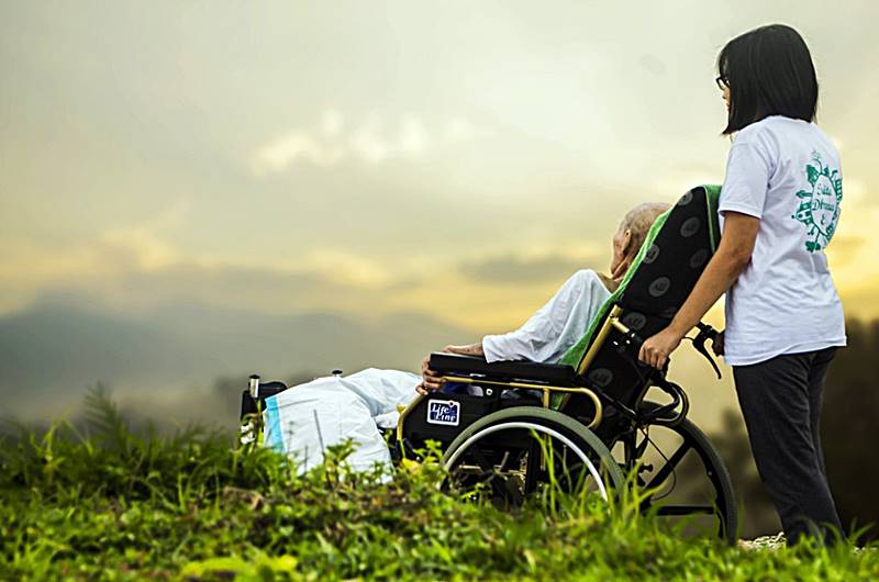 환자가-누워있는-휠체어를-보호자가-간호하는-모습