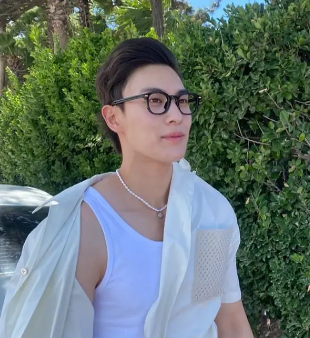 솔로지옥 3 - 앞을 채우지 않은 셔츠 안 흰색 나시티를 입고 흰색 목걸이를 한채 검은색 두꺼운 테 안경을 쓰고 미소짓는 최민우