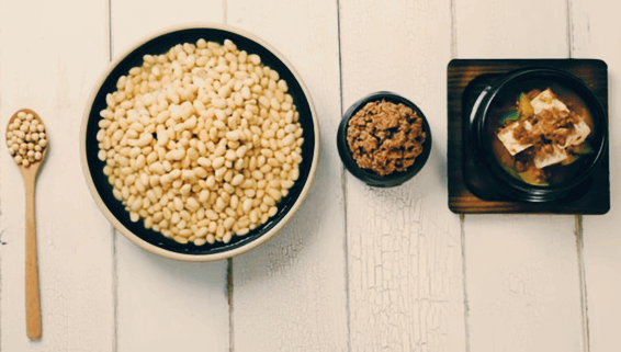 나무 탁자 위에 메주콩을 담은 숟가락, 메주콩 한 사발, 된장 한 그릇, 된장국 한 뚝배기가 나란히 있다.