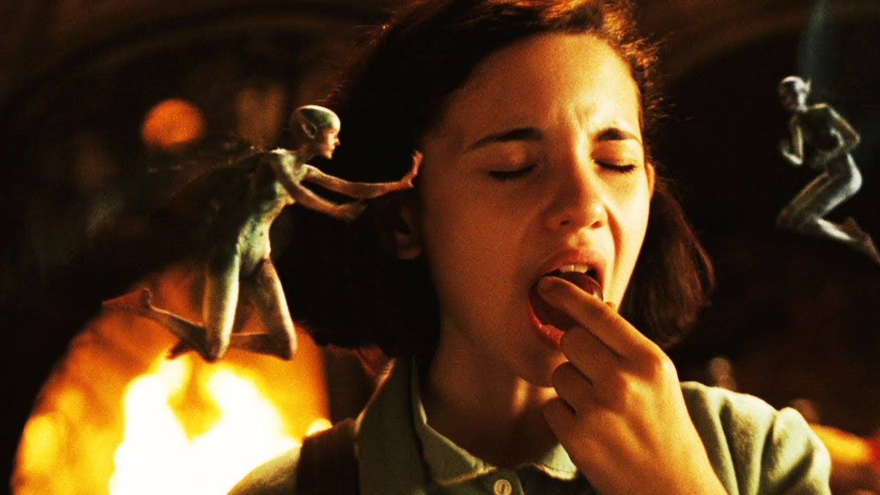 영화 판의 미로에서 여주인공이 눈을 감고 손가락에 무언가를 집어넣는 장면, 주변에 요정들이 날아다니는 모습