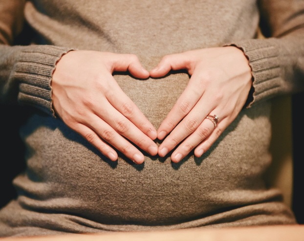 임신부가 배 위에 손으로 하트를 그리고 있습니다.