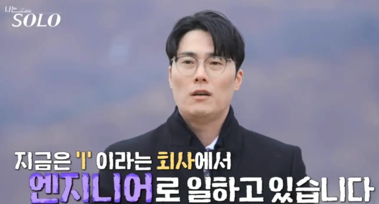 뒷 자연배경 검은 코트를 입고 말하는 영철 아래 흰색과 보라색이 섞인 글씨 지금은 I 이라는 회사에서 엔지니어로 일하고 있습니다.