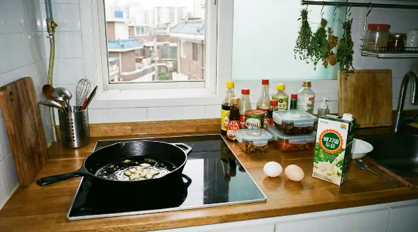 부엌 인덕션 위 프라이펜이 있고, 그 옆에 달걀과 두유가 놓여 있음.