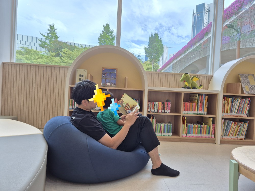 30개월 아기가 도서관 빈백 의자에서 아빠 품에 안겨 진지하고 집중력 있게 책을 읽는 모습