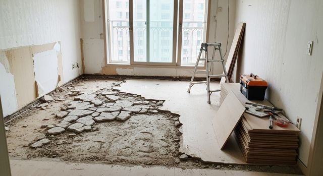 한국 아파트 거실 바닥 철거 후 콘크리트 바닥과 공사 도구가 보이는 리모델링 현장