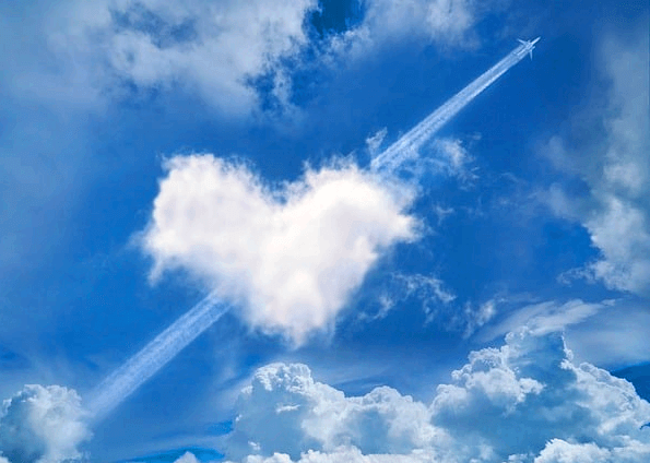 파란 하늘에 하트 모앵의 커다란 하얀 구름이 있다. 그 사이로 하늘 높이 비상하는 작은 비행기가 있다.