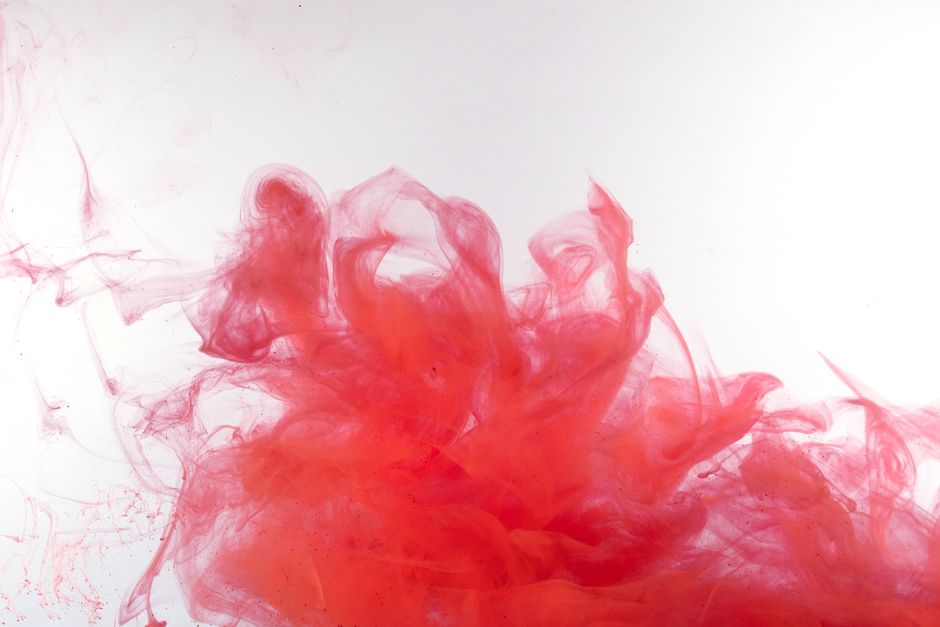 Artistic shot of red ink swirling in clear water, creating fluid patterns.