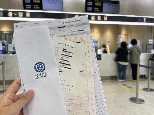 병원 원무과 창구 앞에서 진료비 영수증과 진단 관련 서류를 수령한 모습