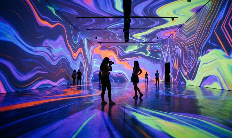 화려한 형광빛 물결무늬의 미디어 아트가 공간을 가득 채운 미술관에서 관람객들이 사진을 찍고 있는 모습