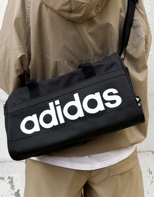 검은색-아디다스-더블백을-메고있는-사람의-뒷모습-흰식-영어로-adidas-라고-크게-써있음-가방을-메고-있는-사람은-브라운-얇은-점퍼를-입고-있음