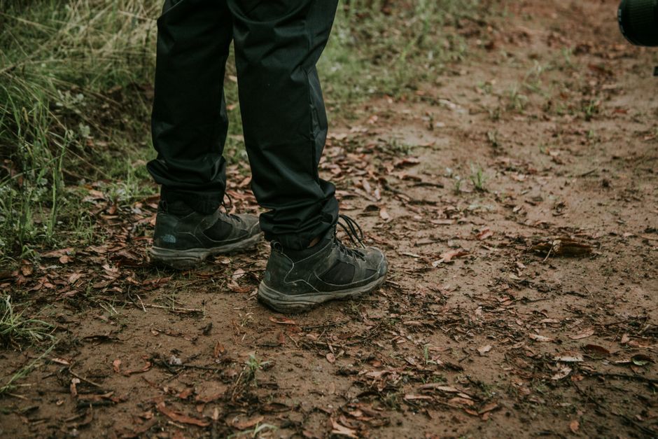 Close-up of legs in black pants and sneakers on a muddy forest path.