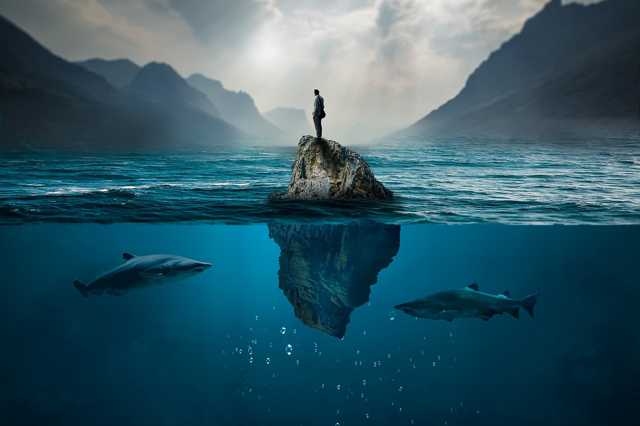 섬에 있는 한 사람을 노리고 있는 바다 속 상어 두 마리