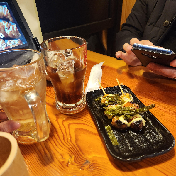 테이블 위에 떡꼬치 두 개와 하이볼 두 잔이 놓여 있다.