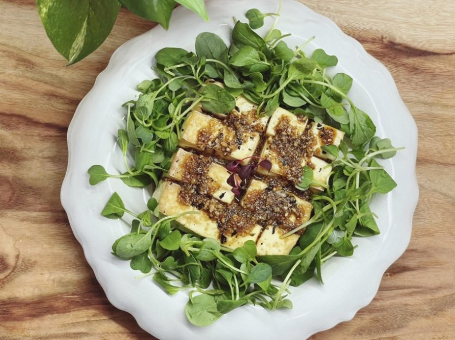 하얗고 동그란 그릇에 야채를 가득 깔아놓고 그 위에 두부를 썰어 놓은 것을 놓아두고 그 위에 참깨간장을 뿌려 놓은 것을 찍은 사진