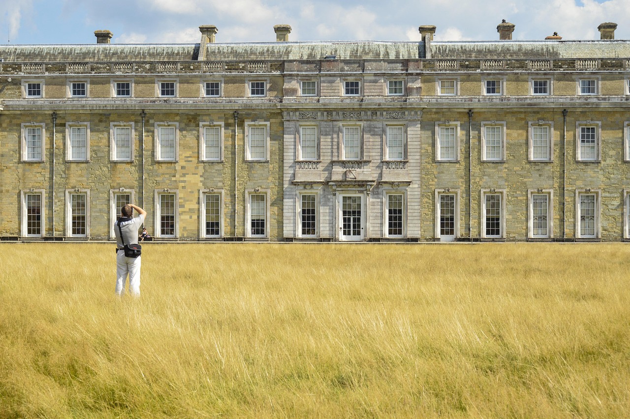 넓은 잔디밭 앞에서 영국 잉글랜드의 National Trust 소속 대저택을 촬영하는 여행자