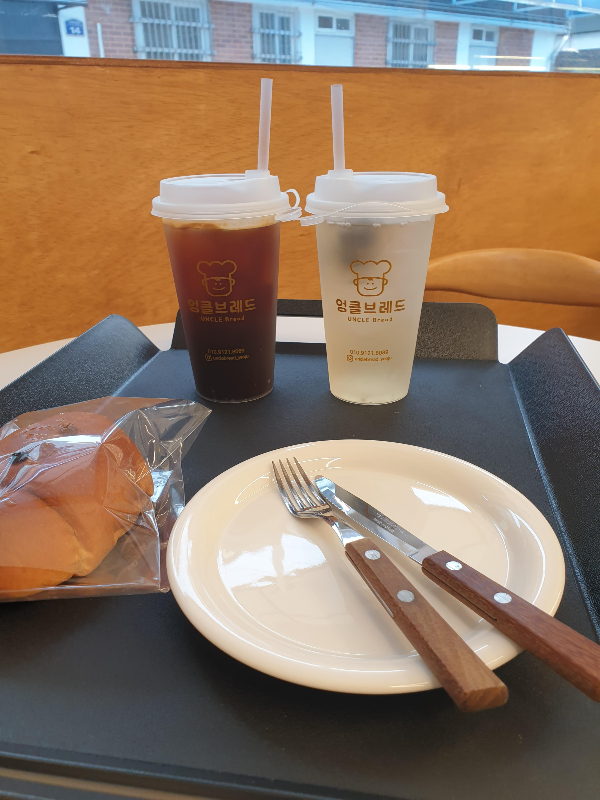 테이블 위에 놓인 트레이 위에 빵과 두 잔의 음료가 올려져 있다.