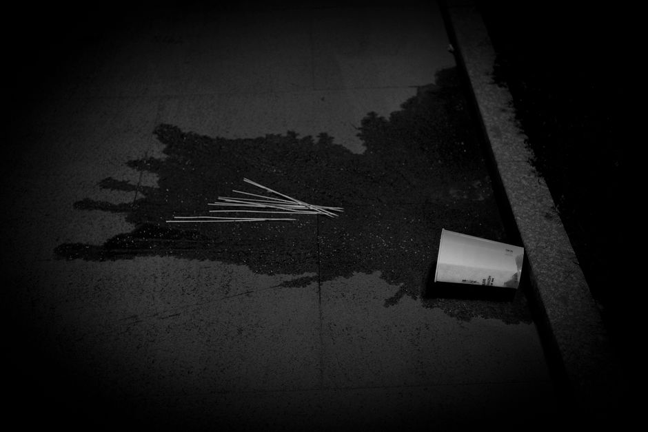 Black and white image of a spilled drink on a pavement with an empty cup lying nearby.