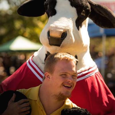 소머리 인형을 쓴 사람에게 안겨 웃고 있는 다운증후군 남자