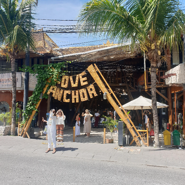 입구에 고객들 몇 명이 서있다. 강렬한 햇빛 때문에 손으로 하늘을 가리고 있다.