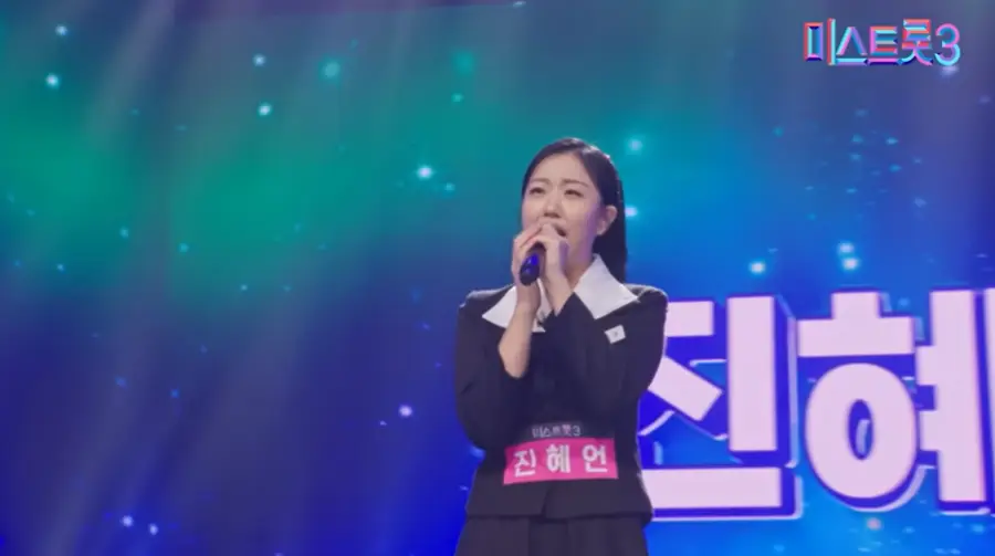 미스트롯3- 흰 카라가 달린 70년대 교복을 입고 배부분 분홍색 진혜언 이름표를 달고 관중을 바라보며 두손으로 마이크를 꼭 쥔채 노래하는 진혜언 출연자