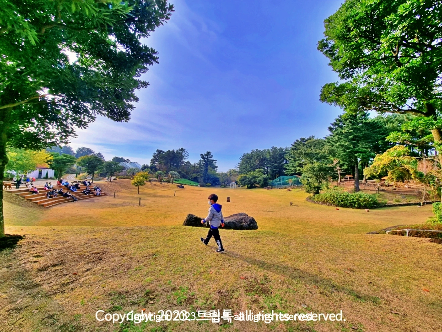 뒤로 넓은 잔디광장이 있고 그 앞에 아이가 걸어간다