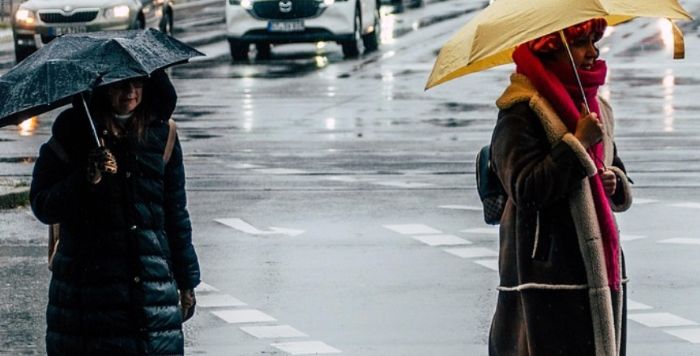 장마철 빗속 도로에서 우산을 쓰고 걷고 있는 두 여성. 도로 위 빗물과 교통량 속 장마철 보행자 안전을 상징하는 장면.