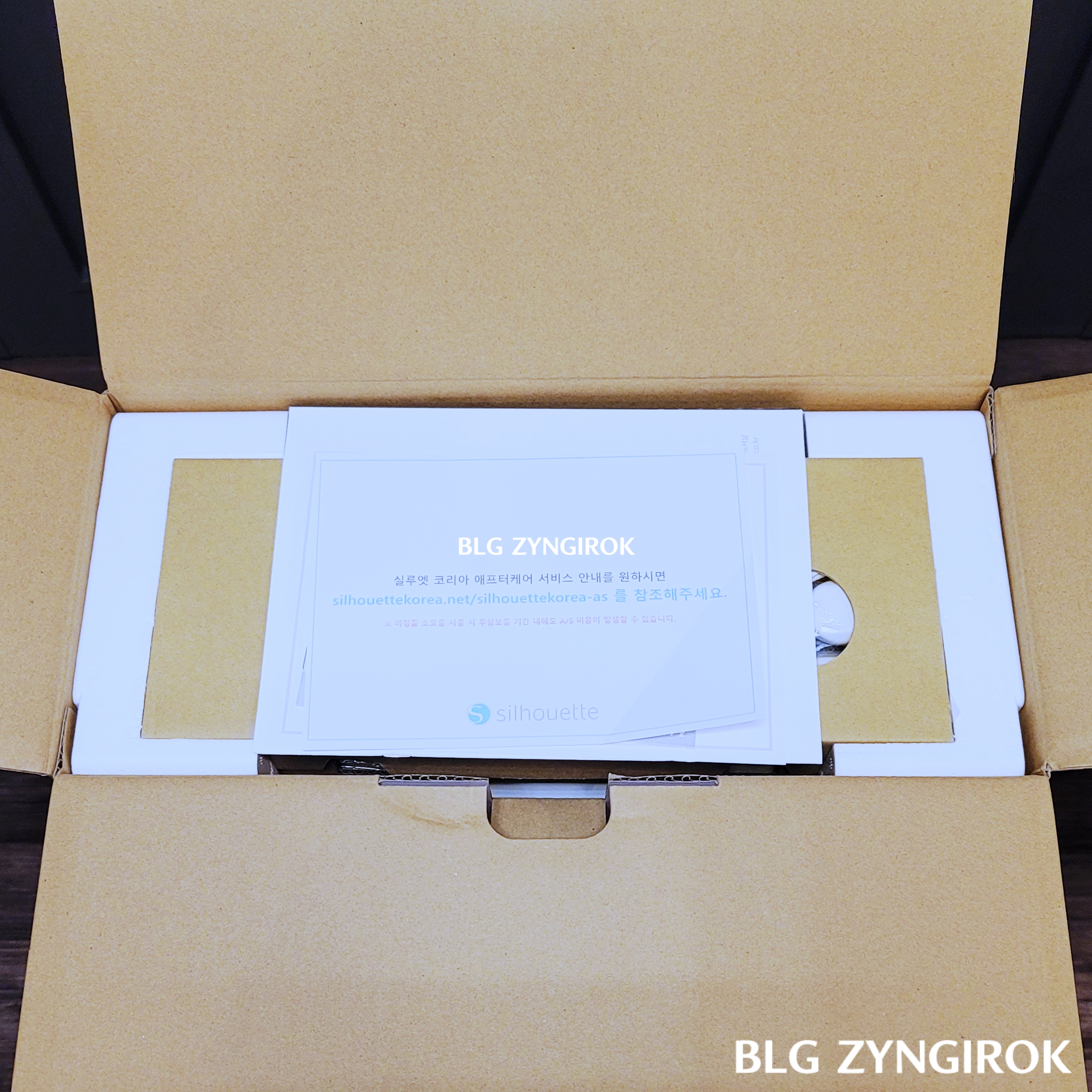 포트레이트3-박스를-열었을때-모습이다.-제품위에-종이들이-놓여있다.