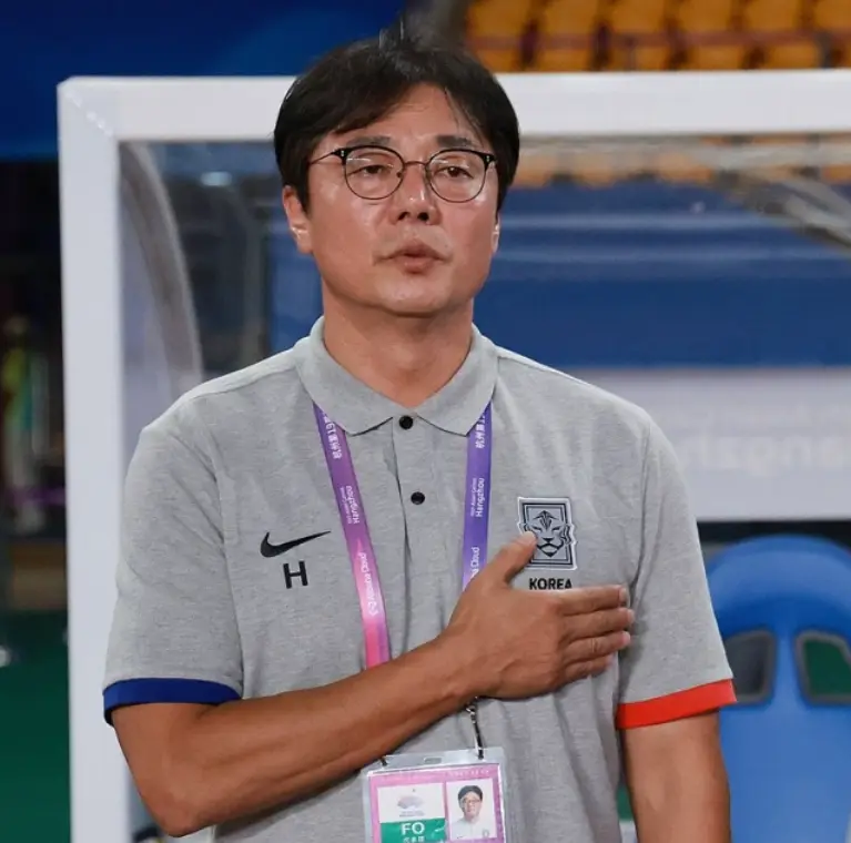 황선홍- 축구장 흰색반팔티 분홍색 목걸이 형 이름표를 목에걸고 오른손을 왼쪽가슴에 댄채 애국가를 부르는 황선홍 감독