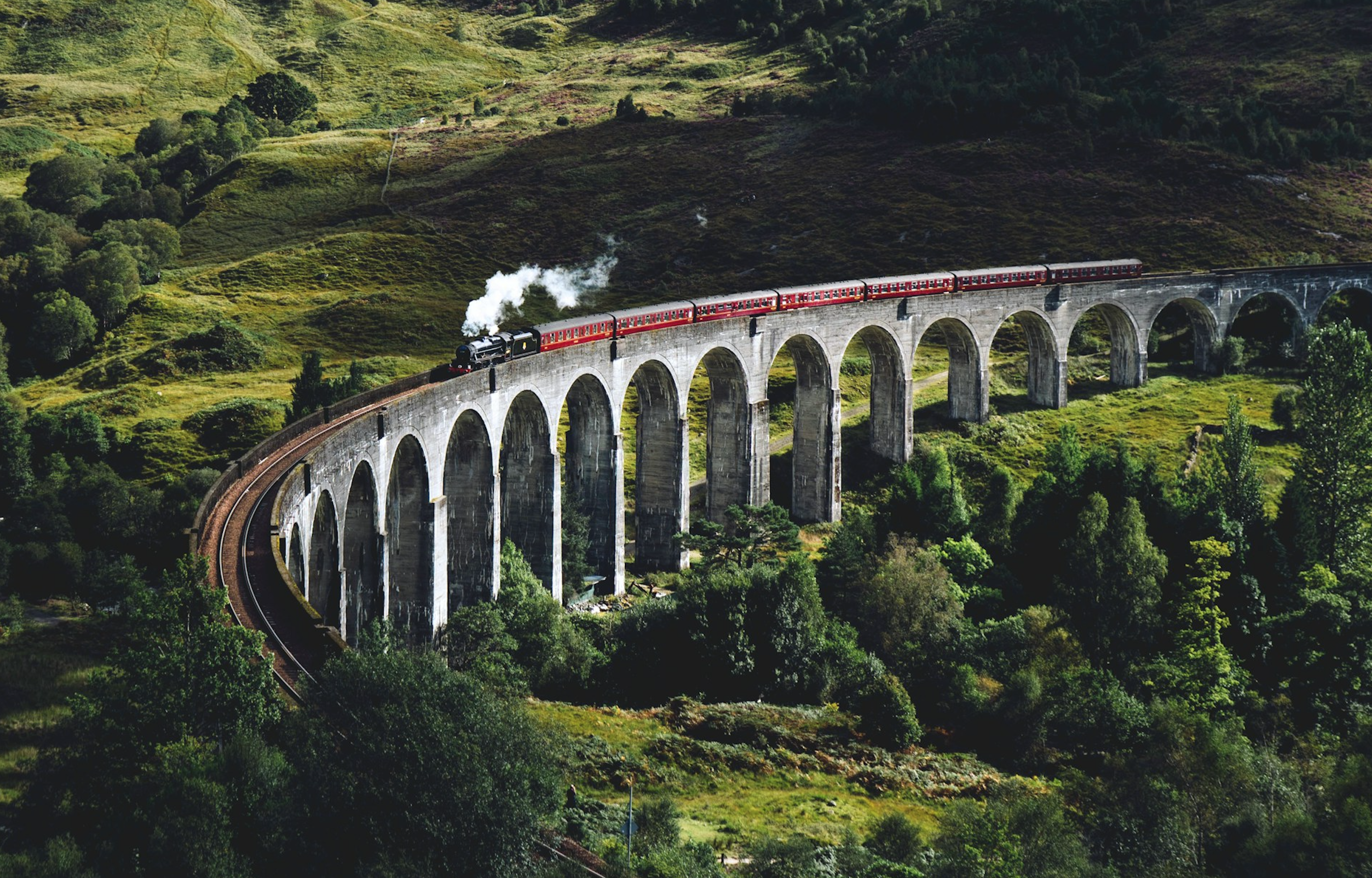 A classic steam train crossing the iconic Glenfinnan Viaduct amidst the lush green hills of Scotland