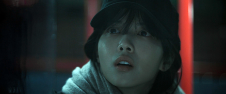 검은 모자를 쓴 여성이 어두운 공간에서 놀란 표정을 짓는 모습