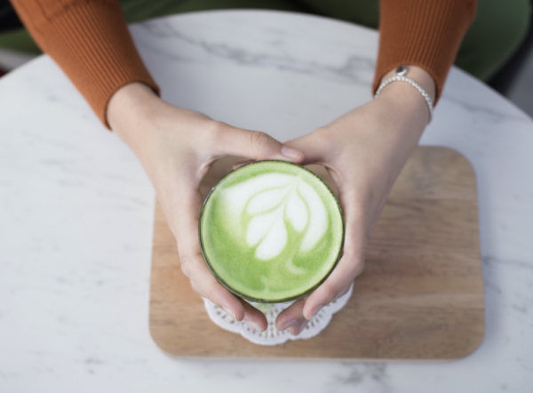 테이블 위에서 말차 라테가 담긴 커피잔을 두손으로 잡고 있다.