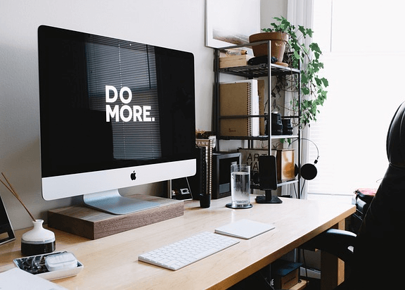 책상 위에 커다란 검정 모니터를 가진 컴퓨터가 있고, 책 상위에는 물이 담긴 투명 유리컵과 책곶이가 있다.