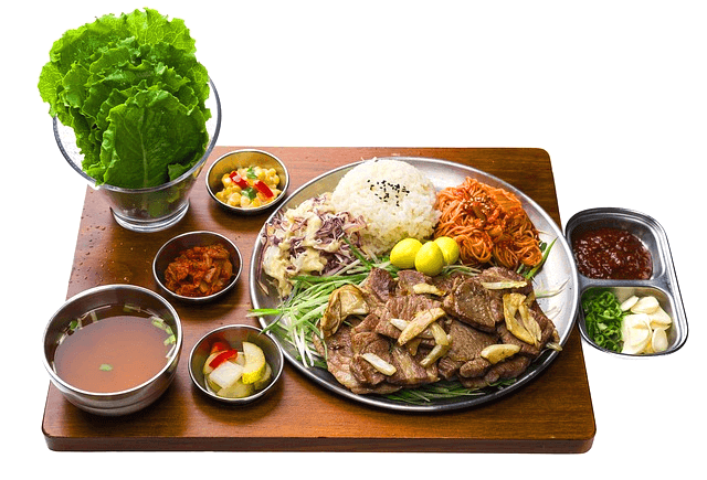 나무 탁자에 한끼 식사가 있다. 둥그런 양은 접시에 흰밥, 고기, 비빔국수가 있도 왼쪽 유리컵엔 상추가 있다. 주변엔 국과 쌈장 등이 있다.