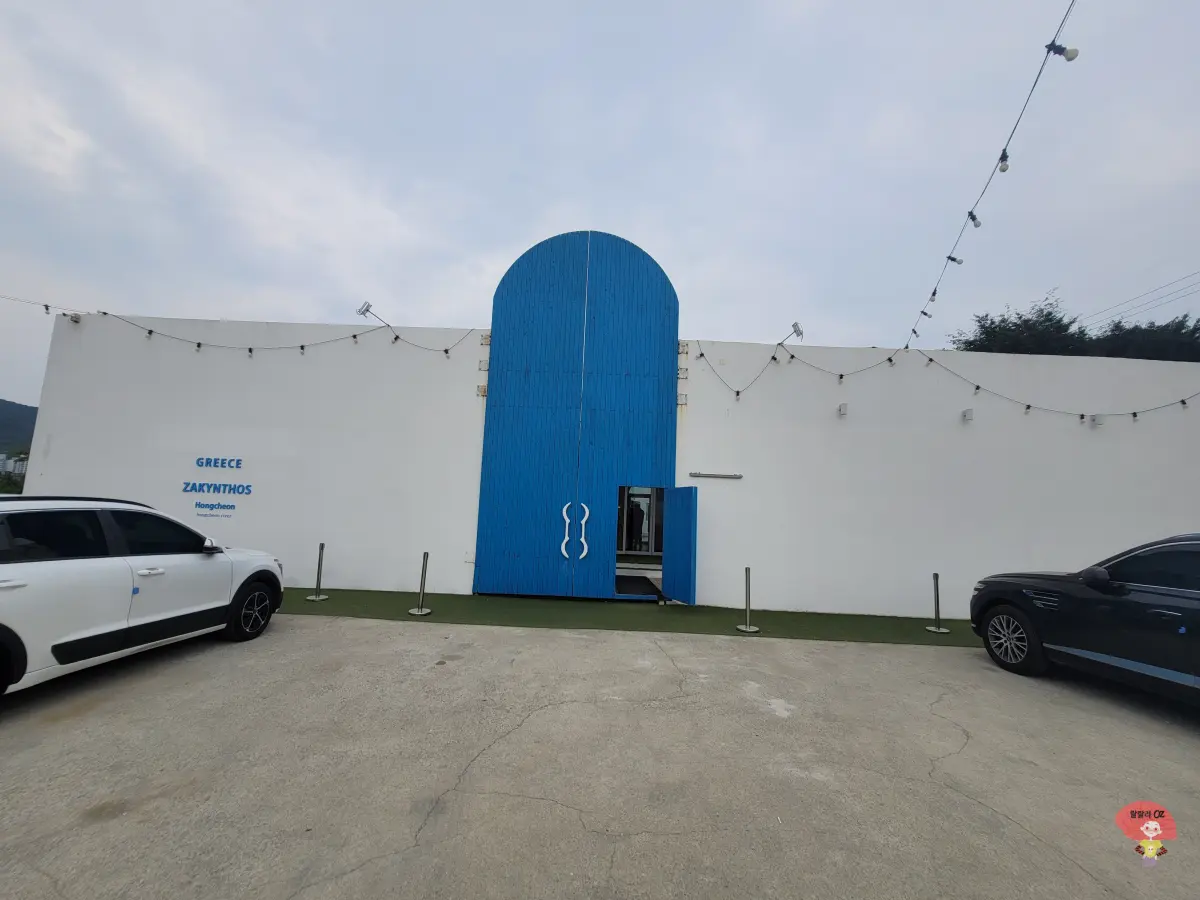 강원도-홍천-카페-테사로바-파란-나무문을-지나-하얀-벽과-붉은-아치문이-이어진-그리스-자킨토스-풍의-카페입구-풍경