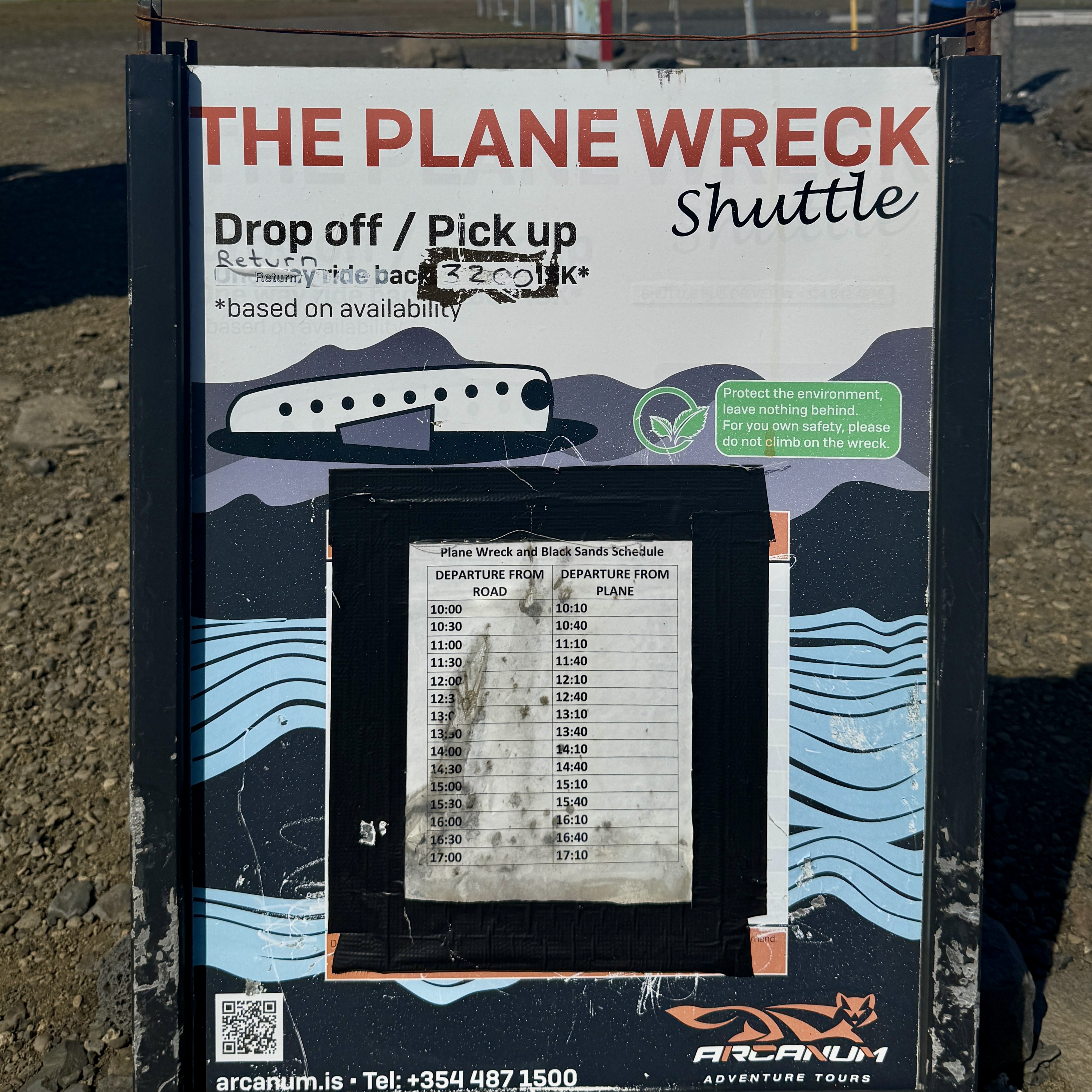 비행기 잔해(The Plane Wreck) 셔틀 안내 표지판입니다. 승하차 지점과 셔틀 시간표가 표시되어 있으며, 환경 보호와 안전을 위해 잔해물에 올라가지 말 것을 당부하는 안내문이 포함되어 있습니다. Arcanum Adventure Tours 연락처와 QR코드도 있습니다.