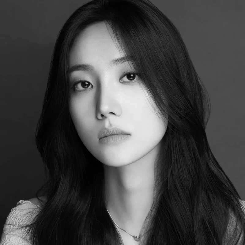 짙은 회색을 배경으로 긴 머리에 밝은 티셔츠를 입고 있는 배우 한재이 프로필 흑백 사진