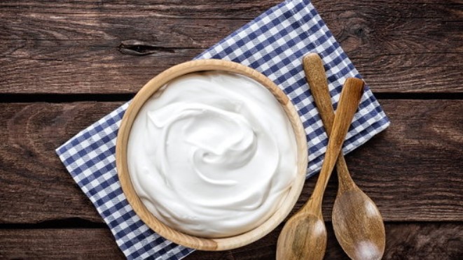 나무 그릇에 흰색 요구르트가 담겨져 있고 옆으로 나무 숟가락과 포크가 놓여져 있다.